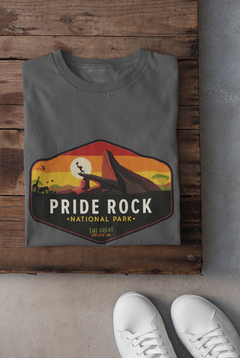 May include: A dark gray t-shirt with a vintage-style graphic of Pride Rock from The Lion King. The graphic features a sunset, a lion, and the text "Pride Rock National Park. The Great Circle of Life."