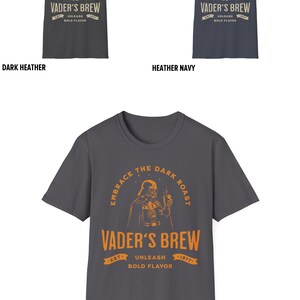 May include: A charcoal grey t-shirt with a graphic of Darth Vader holding a coffee mug. The text reads "Embrace the Dark Roast, Vader's Brew, Est. 1977, Unleash Bold Flavor".