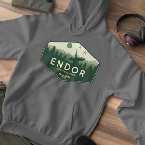 May include: Gray hooded sweatshirt with a green and white graphic of a forest scene with a spaceship and the text "Endor National Park. Home of the Ewoks."