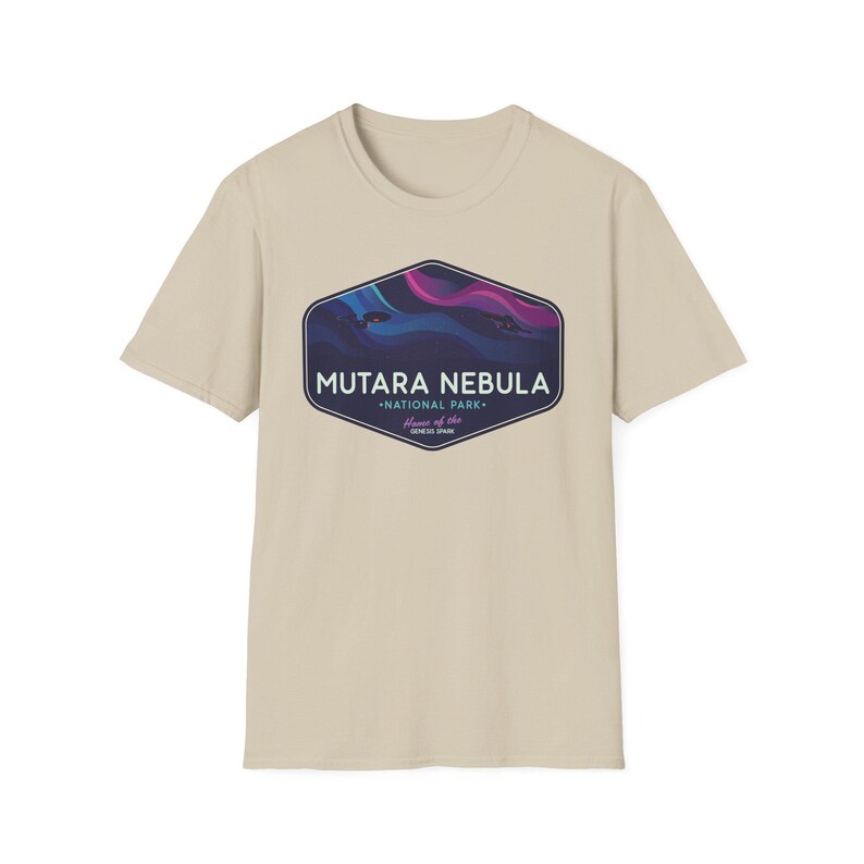 May include: A beige t-shirt featuring a graphic of the Mutara Nebula National Park. The graphic is a dark blue, purple, and pink design inside a dark blue hexagon. The text "MUTARA NEBULA" and "NATIONAL PARK" are also included.