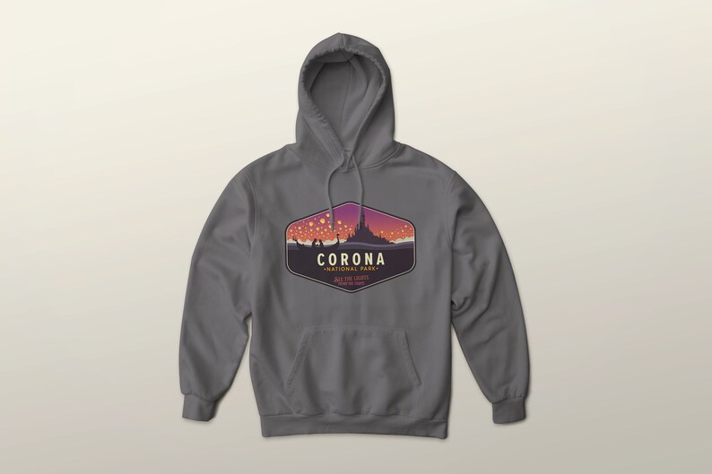 Puede incluir: Una sudadera con capucha gris con un bolsillo delantero y un cord&oacute;n. La parte delantera presenta un gr&aacute;fico de un castillo y linternas flotantes, con el texto "CORONA NATIONAL PARK" y "SEE THE LIGHTS".
