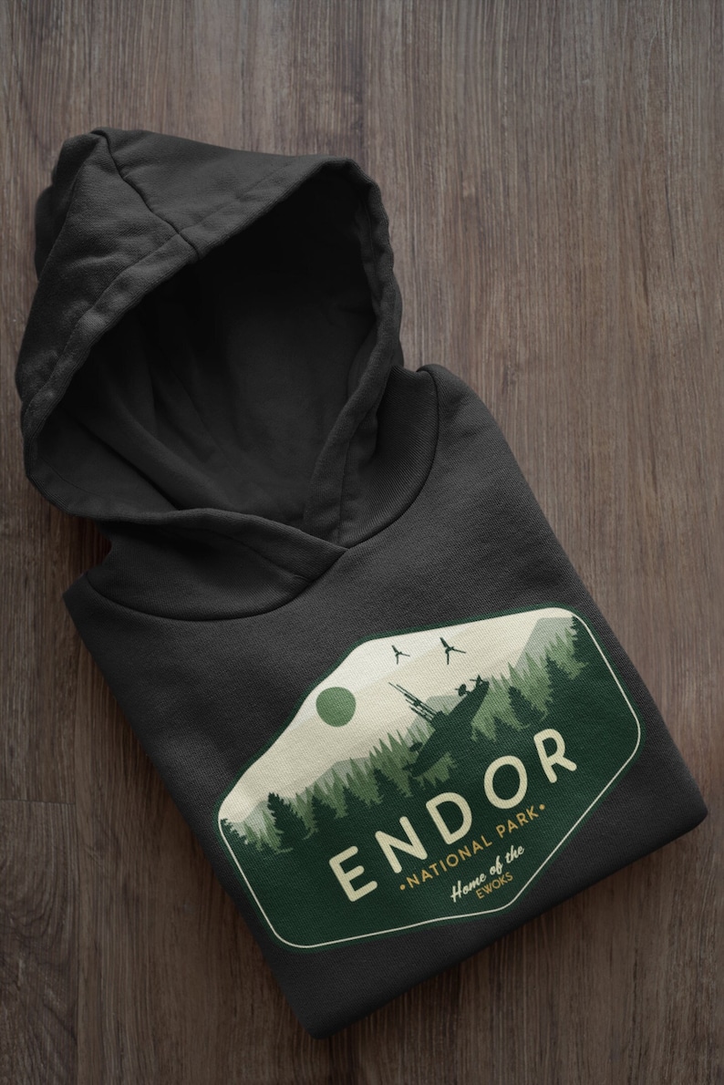 May include: Black hooded sweatshirt with a green and white graphic design of a forest scene with a spaceship in the background. The graphic says "Endor National Park - Home of the Ewoks".