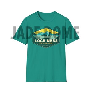 May include: Teal blue t-shirt with a vintage-style graphic of a Loch Ness Monster in a lake with the text "Loch Ness National Park. Explore the Depths of Legend."