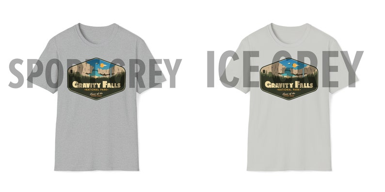 K&ouml;nnte beinhalten: Zwei T-Shirts in verschiedenen Graut&ouml;nen, beide mit einem Grafikdruck eines Retro-Nationalpark-Logos mit dem Text "Gravity Falls National Park" und einer Illustration einer Bergkette und eines Sees. Das Logo hat eine sechseckige Form mit gelbem Rand und braunem Hintergrund.