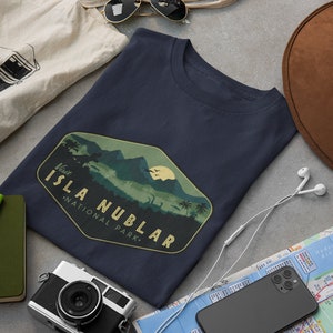 K&ouml;nnte beinhalten: Ein marineblaues T-Shirt mit einer Vintage-Grafik einer Bergkette und dem Text "Besuchen Sie den Isla Nublar National Park."