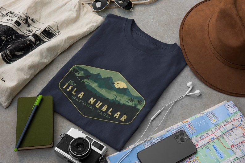 K&ouml;nnte beinhalten: Ein marineblaues T-Shirt mit einer Vintage-Grafik einer Bergkette und dem Text "Besuchen Sie den Isla Nublar National Park."