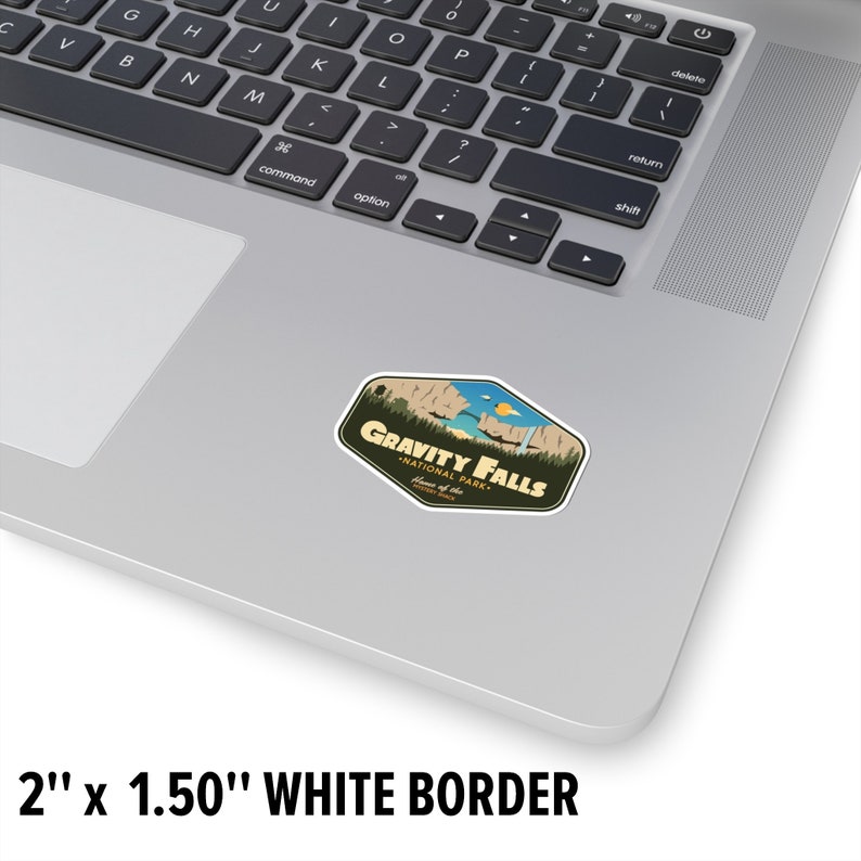 May include: A sticker featuring a retro-style illustration of a mountain range with a waterfall, with the text "Gravity Falls National Park" in a brown banner. The sticker is 2 inches by 1.5 inches and has a white border.