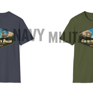 K&ouml;nnte beinhalten: Zwei T-Shirts mit einem Grafikdruck eines Retro-Nationalpark-Logos. Das Logo zeigt eine Bergkette, einen See und den Text "Gravity Falls National Park". Die T-Shirts sind in den Farben Heather Navy und Milit&auml;rgr&uuml;n erh&auml;ltlich.