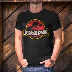 Black unisex T-shirt with the classic Jurassic Park red and yellow dinosaur logo, retro 90s nostalgia graphic tee for men and women.