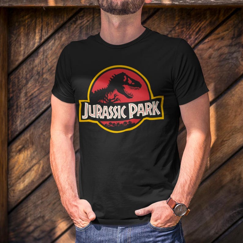 Black unisex T-shirt with the classic Jurassic Park red and yellow dinosaur logo, retro 90s nostalgia graphic tee for men and women.