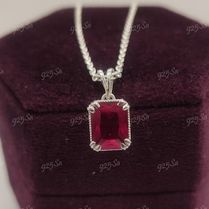 May include: A silver chain necklace with a red gemstone pendant. The pendant is a square shape with a silver border.