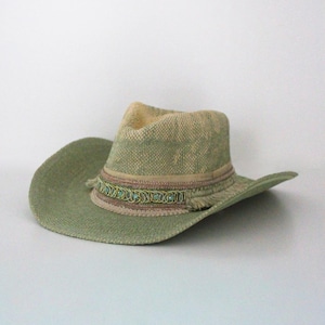 May include: A light green cowboy hat with a wide brim. The hat features a decorative band with fringe and turquoise-colored accents. The hat is made of woven material and has a neutral-colored crown.