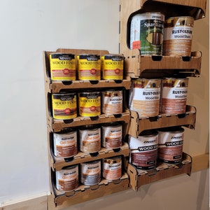 May include: A wooden shelf unit with various brands of wood stain and wood finish in cans. The brands include Minwax, Rust-Oleum, and Zinsser. The cans are arranged on shelves in a vertical stack.
