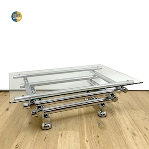 Peut inclure: Table basse moderne avec un plateau rectangulaire en verre et une structure en métal chromé. Le cadre est composé de barres horizontales et verticales, soutenues par des pieds arrondis. Esthétique vintage.