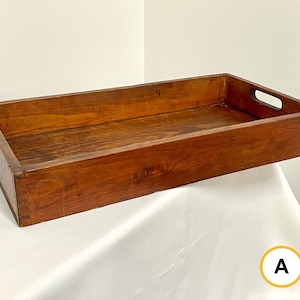 Op de afbeelding: Een rechthoekige houten dienblad met een donkerbruine vlek en twee handvatten aan de zijkanten. Het dienblad staat op een wit oppervlak.