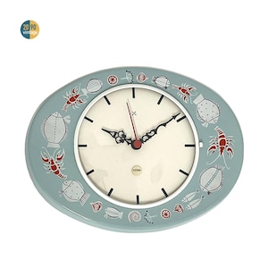 May include: Oval vintage wall clock with a pale blue border and a white clock face. The border features illustrations of sea creatures in red and white. The clock hands are black, and the second hand is red.