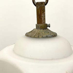 May include: Close-up of a vintage white glass lamp shade with a brass fixture. The shade has a rounded shape and a decorative floral design. The brass components show signs of age and wear, adding to its antique charm.