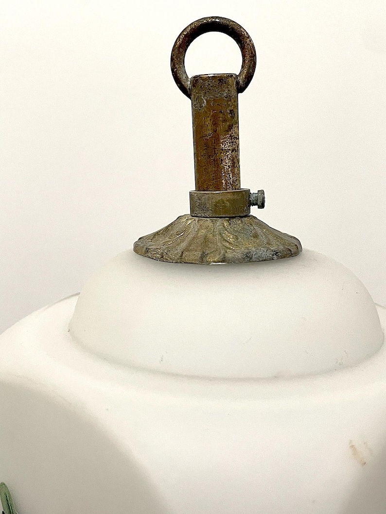 May include: Close-up of a vintage white glass lamp shade with a brass fixture. The shade has a rounded shape and a decorative floral design. The brass components show signs of age and wear, adding to its antique charm.