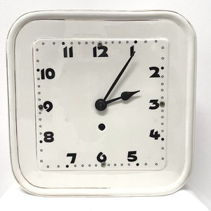 Könnte beinhalten: Weiße quadratische Uhr mit schwarzen römischen Ziffern und schwarzen Zeigern. Das Zifferblatt der Uhr hat einen weißen Hintergrund mit schwarzen Markierungen.