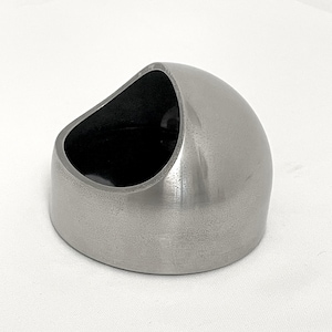 May include: A silver-toned metal object with a smooth, rounded dome shape and a slanted, open top. The exterior has a brushed metallic finish, while the interior cavity is dark and hollow, featuring a clean, curved edge along the slanted opening.