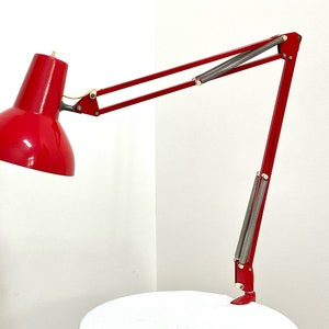 May include: A red metal desk lamp with a long, adjustable arm. The lamp has a round, red shade and a silver base.