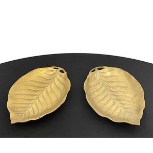 Puede incluir: Dos platos de servir dorados en forma de hoja con un diseño texturizado. Los platos son de latón y tienen un acabado brillante.