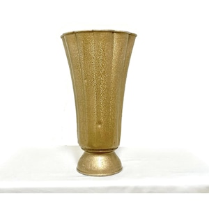 Può includere: Un vaso alto in metallo color oro con un bordo svasato e smerlato, caratterizzato da una finitura testurizzata e maculata. Il corpo presenta pannelli verticali scanalati che si restringono verso una base circolare a piedistallo, creando una forma simmetrica.