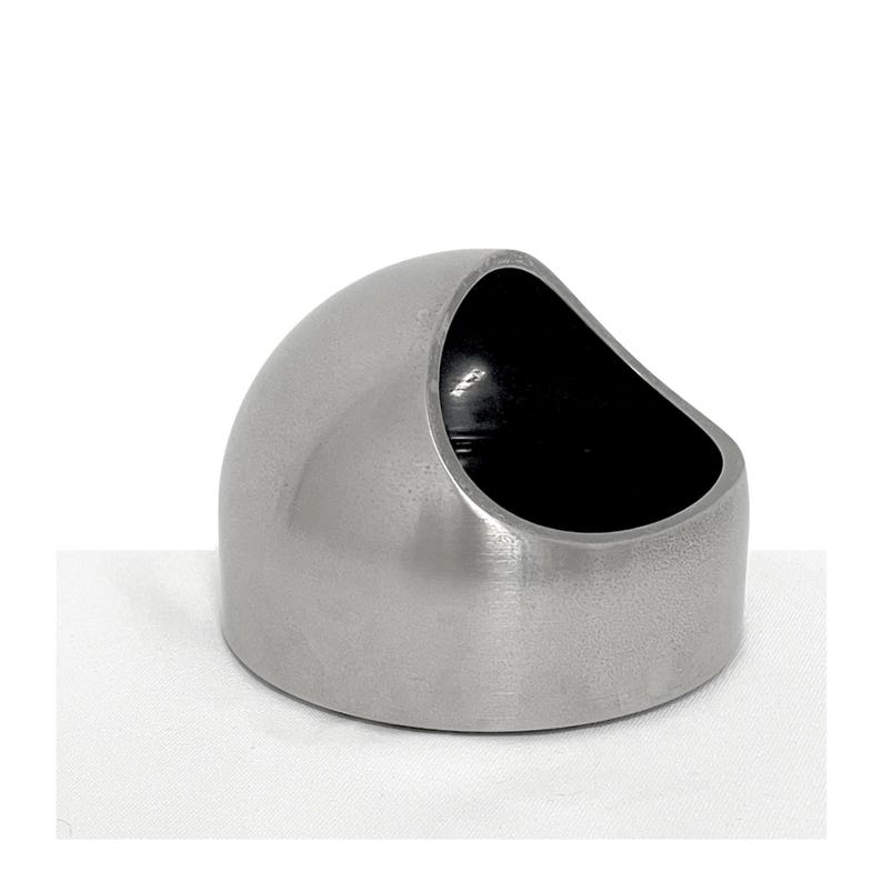 May include: A dome-shaped container with a brushed silver metallic exterior and a smooth, dark interior. The object features a slanted, circular opening at the top, creating a hollow basin with a flat base and a curved, solid outer wall.