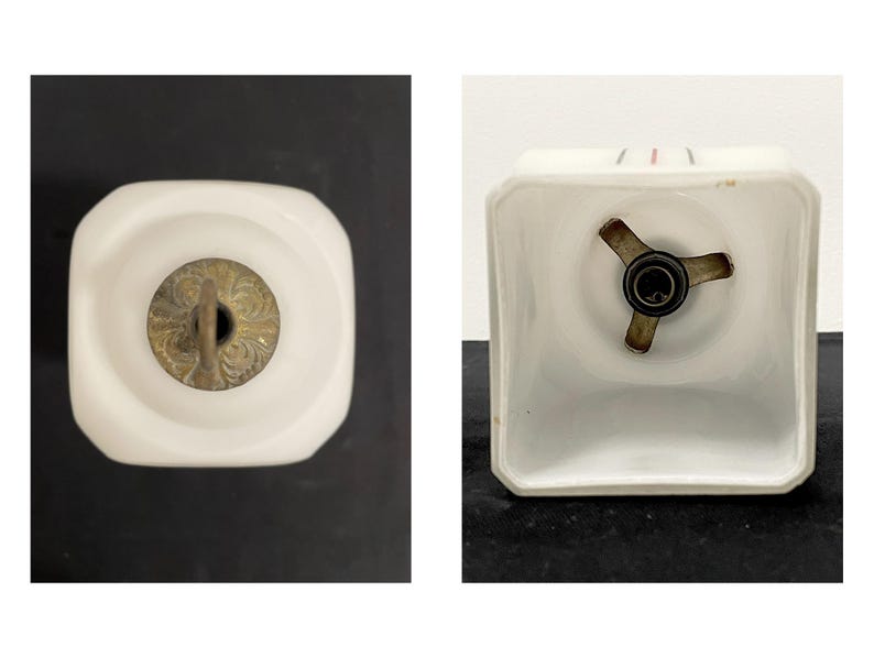 May include: Two views of a white, square-shaped light fitting. One view shows the top with a brass-coloured decorative element. The other view shows the bottom with a three-pronged metal piece and a light bulb socket.
