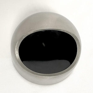May include: A spherical object with a matte silver exterior and a smooth, deep black interior. The item features a wide, circular opening cut into the side, revealing the dark, reflective hollow space within the metallic, rounded shell structure.
