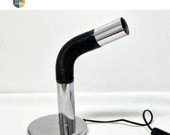 May include: A vintage chrome desk lamp with a flexible black neck and a round base. The lamp has a cylindrical head and a power cord with a switch. The lamp is labeled with the text "20 90 vintage".