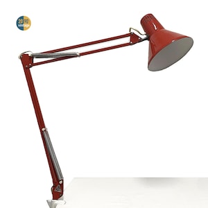 May include: A vintage red desk lamp with a white interior shade. The lamp has an adjustable arm with a spring mechanism and a clamp base. The lamp is labeled "20 90 vintage".