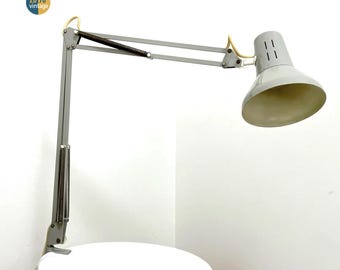 May include: A vintage gray desk lamp with a spring-loaded arm and a conical shade. The lamp has a classic design, with a pivoting head and adjustable arm. The lamp is mounted on a white surface. The lamp is labeled "20 90 vintage".