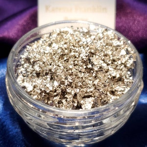 May include: A glass jar filled with silver flakes. The flakes are shiny and metallic, and they are arranged in a random pattern.