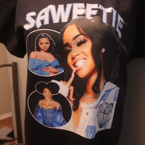 May include: Black t-shirt with a graphic print of three women. The text "SAWEETIE" is printed in rhinestones on the top of the shirt.