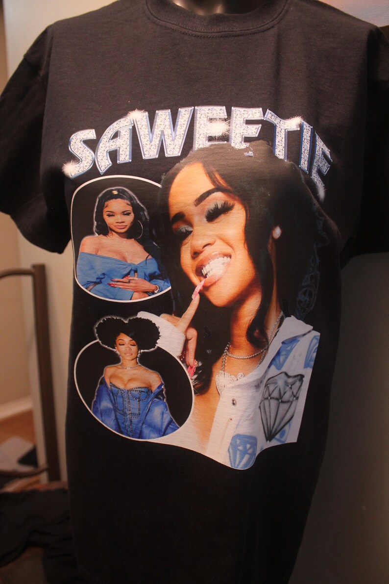 May include: Black t-shirt with a graphic print of three women. The text "SAWEETIE" is printed in rhinestones on the top of the shirt.