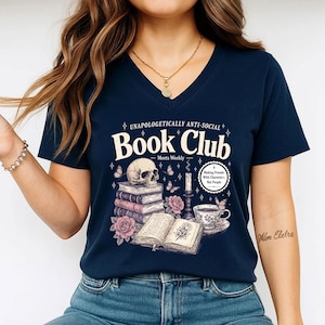 A woman wearing a navy blue t-shirt with a graphic design featuring a skull, books, and other symbols, along with text that reads "Book Club" and "Making friends, not enemies".