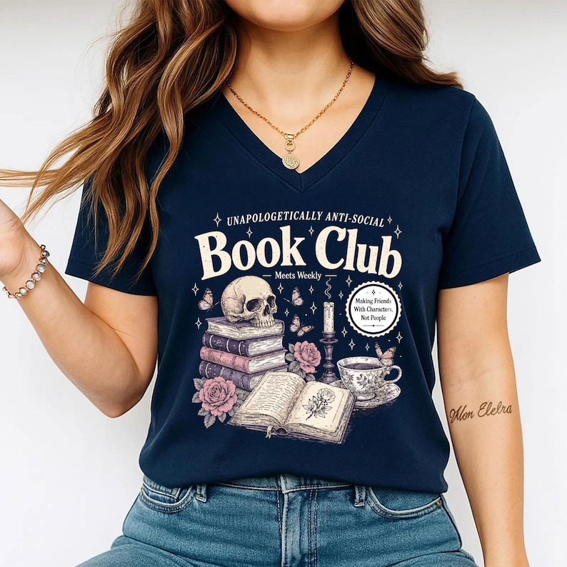 A woman wearing a navy blue t-shirt with a graphic design featuring a skull, books, and other symbols, along with text that reads "Book Club" and "Making friends, not enemies".