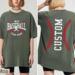 A woman wearing a green t-shirt with a baseball design and text printed on it.