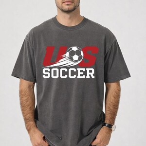 A man wearing a gray t-shirt with the text "U.S. SOCCER" printed on it.