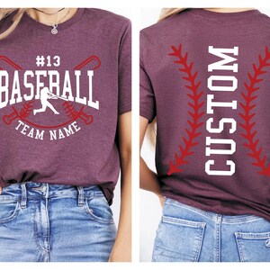 a person wearing a maroon t-shirt with a baseball design and text, as well as a pair of blue jeans.