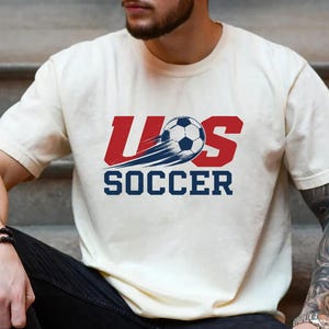 A man wearing a white t-shirt with a graphic of a soccer ball and the text "U.S. SOCCER" printed on it.