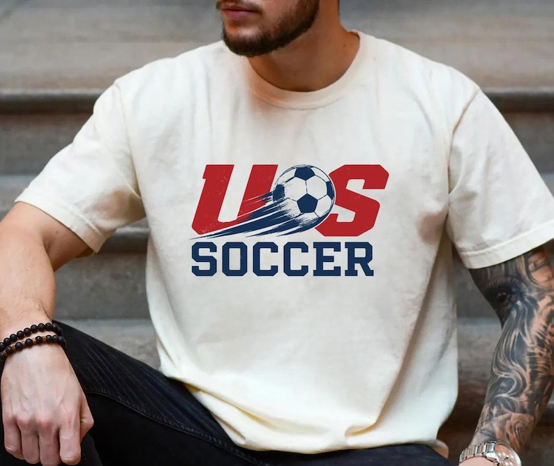 A man wearing a white t-shirt with a graphic of a soccer ball and the text "U.S. SOCCER" printed on it.