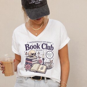 A woman wearing a white t-shirt with a graphic design and holding a drink.