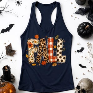 May include: A navy blue racerback tank top featuring the word FALL printed in large block letters. Each letter has a distinct pattern: floral with orange flowers, leopard print, red and white buffalo plaid, and black polka dots on cream.