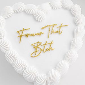 May include: White heart-shaped cake with gold glitter frosting that says "Forever That Bitch".