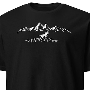 Puede incluir: Camiseta negra con un gráfico blanco de un lobo aullando frente a una cordillera. El diseño es una ilustración minimalista, perfecta para los amantes del aire libre. La camiseta está hecha de un material suave y cómodo.