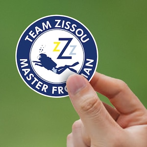 Puede incluir: Una pegatina redonda azul y amarilla con el texto "Team Zissou Master Fro-