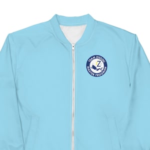 May include: Light blue bomber jacket with a white interior and a full-length zipper. The jacket features a circular emblem on the chest with the text "TEAM ZISSOU MASTER FROGMAN" and a stylized "Z" in the center. The jacket is a solid light blue color.