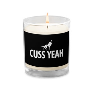 Könnte beinhalten: Ein schwarzes Glas-Kerzengefäß mit einer weißen Wolfgrafik und dem Text "CUSS YEAH". Die Kerze ist angezündet und die Flamme ist sichtbar.